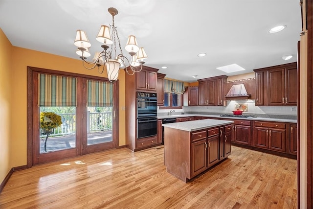 kitchen featuring light wood-type flooring, black appliances, decorative light fixtures, an inviting chandelier, and a center island