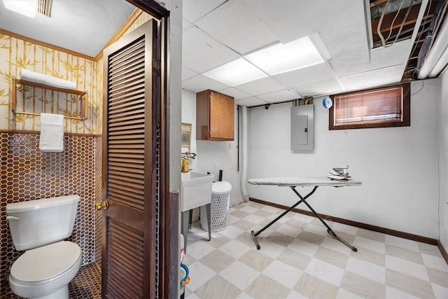 bathroom with a paneled ceiling, toilet, and electric panel