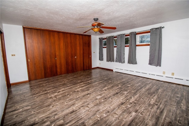 spare room with wood walls, dark wood-type flooring, a baseboard heating unit, ceiling fan, and a textured ceiling