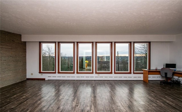132 Random Rd, Corry, PA 16407 - unfurnished living room with a textured ceiling, wood finished floors, a desk, brick wall, and plenty of natural light