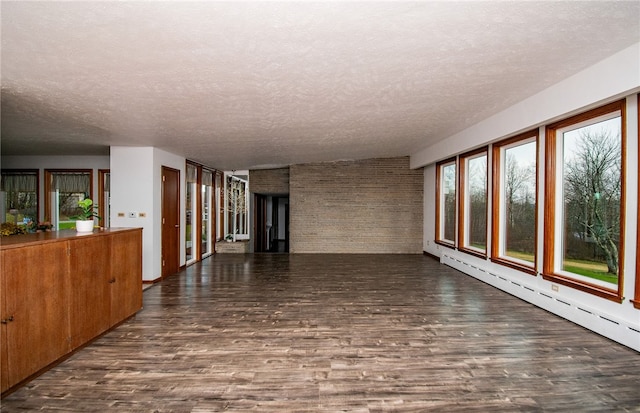 empty room with a textured ceiling, dark wood-type flooring, and a baseboard heating unit