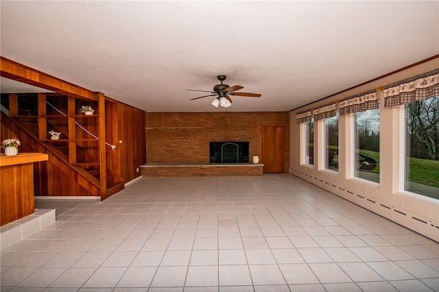 unfurnished living room with ceiling fan, light tile patterned flooring, wooden walls, and a brick fireplace