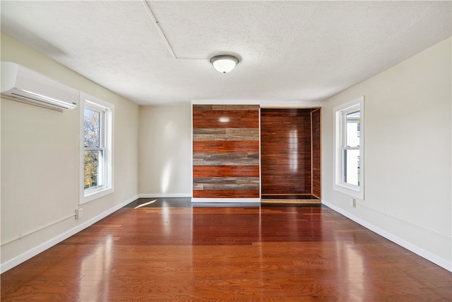 spare room featuring wood-type flooring, an AC wall unit, and a textured ceiling