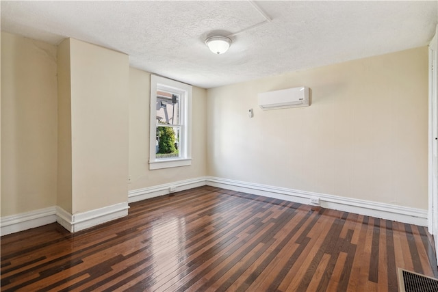 unfurnished room with dark hardwood / wood-style flooring, a textured ceiling, and a wall unit AC