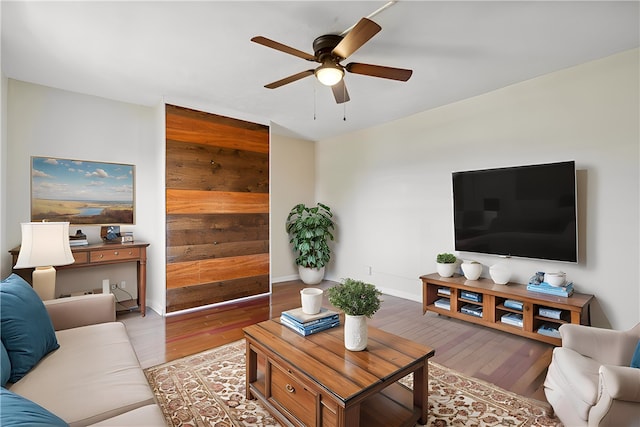 living room with hardwood / wood-style flooring, ceiling fan, and wooden walls