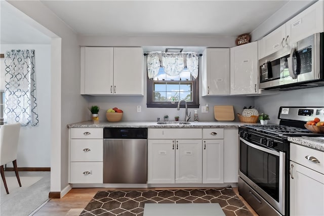 kitchen with sink, light stone countertops, light wood-type flooring, white cabinetry, and appliances with stainless steel finishes