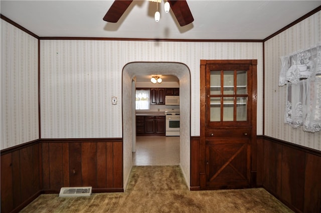 corridor with crown molding, wooden walls, and dark carpet