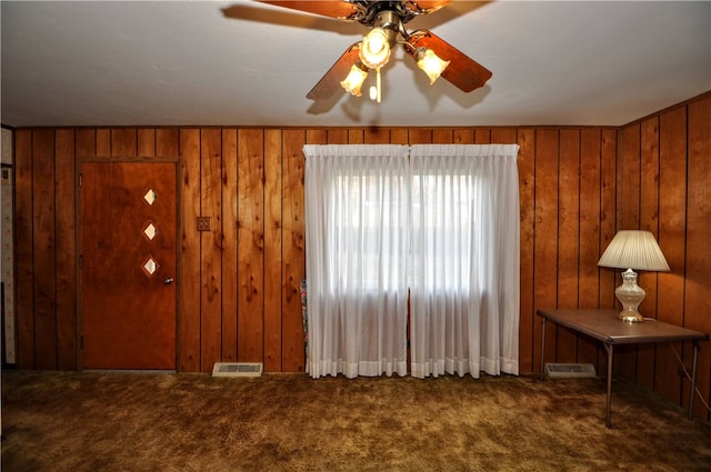 interior space with carpet floors, wooden walls, and ceiling fan