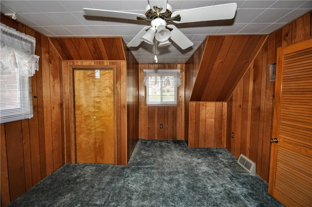 additional living space with ceiling fan, wood walls, and dark colored carpet