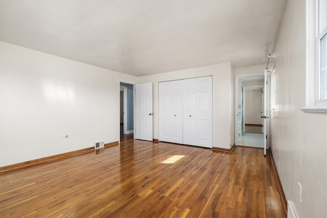 unfurnished bedroom with a closet, wood-type flooring, and baseboard heating