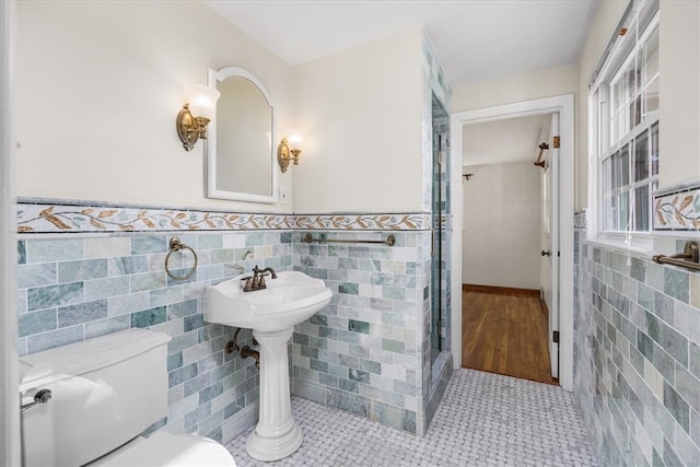 bathroom featuring a shower with door, toilet, tile walls, and tile patterned flooring