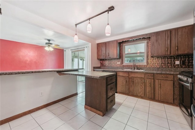 kitchen featuring stainless steel range with gas cooktop, sink, ceiling fan, tasteful backsplash, and decorative light fixtures