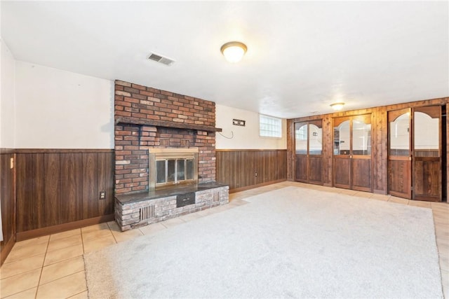 unfurnished living room with a brick fireplace, wooden walls, and light tile patterned flooring