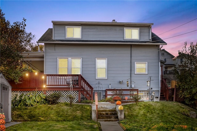 back house at dusk with a lawn and a wooden deck