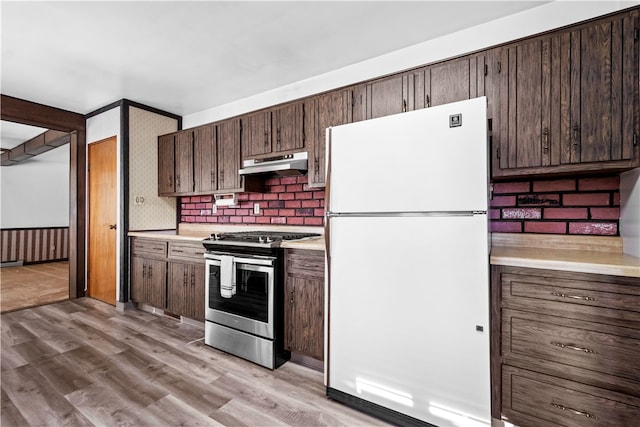 kitchen featuring light wood-type flooring, white refrigerator, dark brown cabinets, decorative backsplash, and stainless steel range