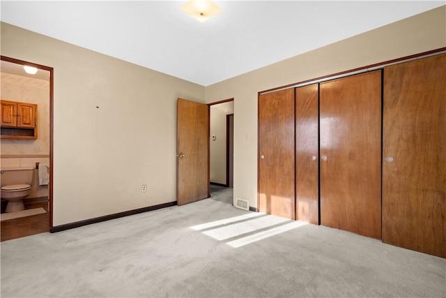 unfurnished bedroom with ensuite bathroom, light colored carpet, and a closet