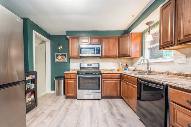 kitchen with appliances with stainless steel finishes, sink, pendant lighting, decorative backsplash, and light hardwood / wood-style flooring