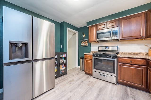 kitchen with appliances with stainless steel finishes, light stone countertops, backsplash, and light hardwood / wood-style floors