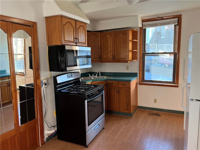 kitchen with sink, vaulted ceiling, appliances with stainless steel finishes, and light hardwood / wood-style flooring