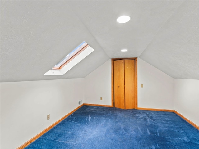 bonus room with lofted ceiling with skylight, dark colored carpet, and a textured ceiling