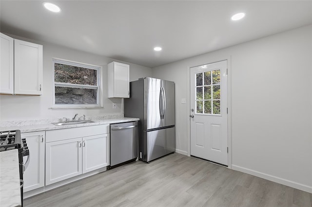 kitchen with light stone countertops, appliances with stainless steel finishes, sink, light wood-type flooring, and white cabinets