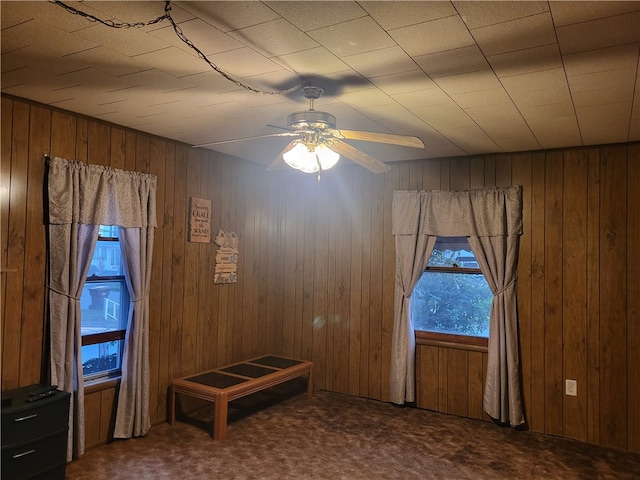 unfurnished room featuring wooden walls, carpet, and ceiling fan