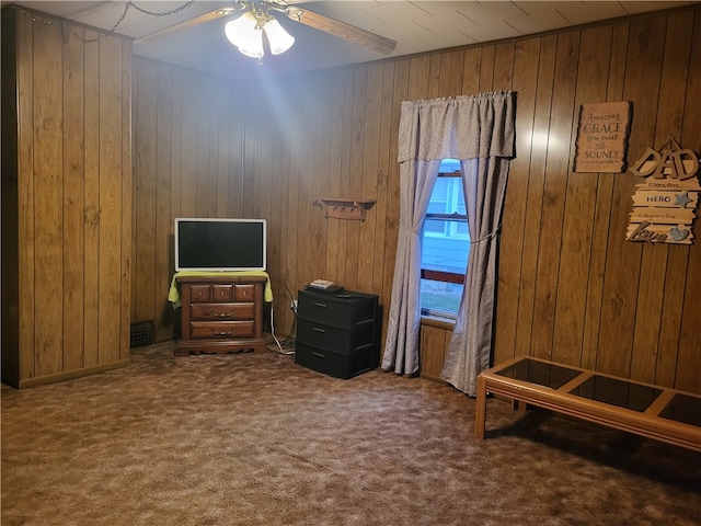 interior space with ceiling fan, carpet flooring, and wooden walls