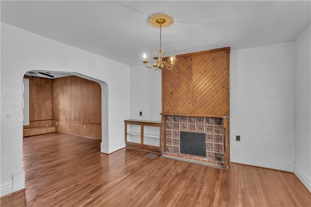 unfurnished living room with a notable chandelier, wooden walls, and wood-type flooring