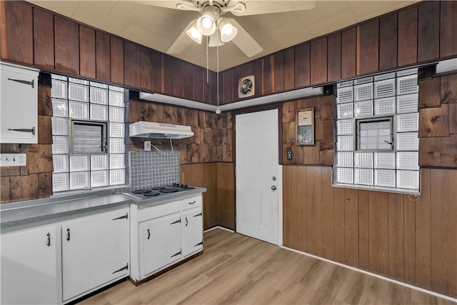 kitchen featuring backsplash, white cabinetry, stainless steel gas stovetop, light hardwood / wood-style flooring, and wooden walls