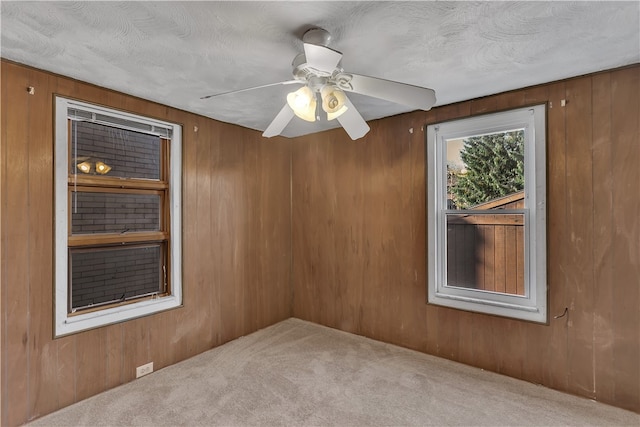 carpeted empty room with ceiling fan, a textured ceiling, and wooden walls