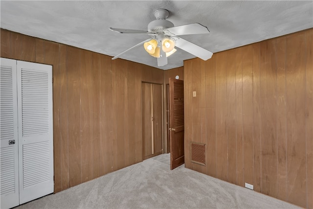 unfurnished bedroom featuring wood walls, light colored carpet, and ceiling fan