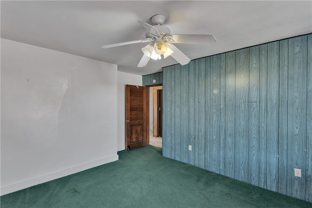 unfurnished room with ceiling fan, wooden walls, and dark carpet