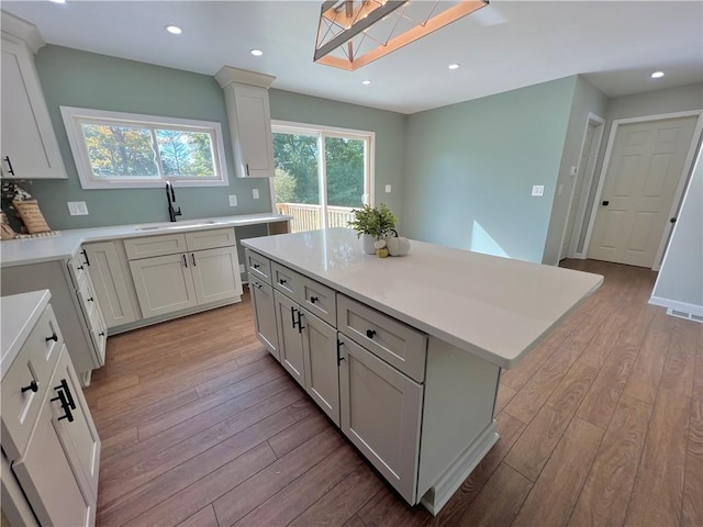 kitchen with light wood-type flooring, white cabinetry, a kitchen island, and sink