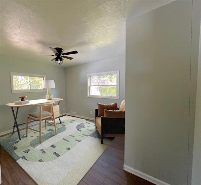 home office with ceiling fan, dark hardwood / wood-style flooring, a healthy amount of sunlight, and a textured ceiling