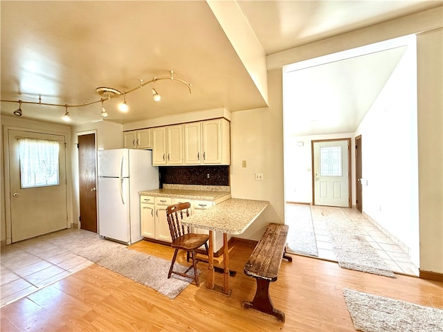 kitchen featuring white fridge, light hardwood / wood-style floors, decorative backsplash, and white cabinetry