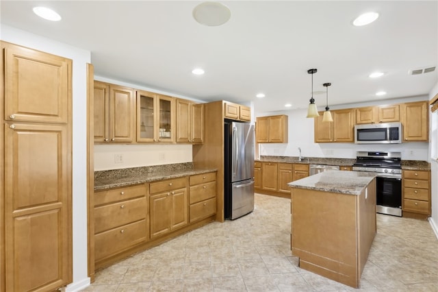 kitchen with stainless steel appliances, sink, stone countertops, pendant lighting, and a center island