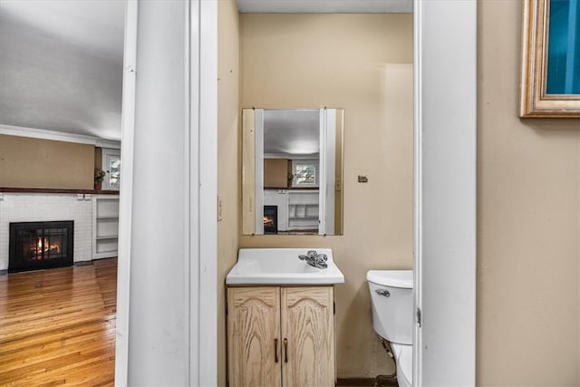 bathroom with vanity, a brick fireplace, wood-type flooring, and toilet