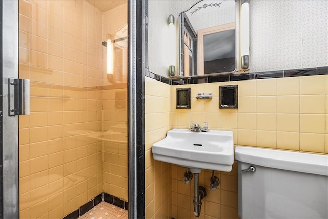 bathroom featuring a tile shower, toilet, tile walls, and sink