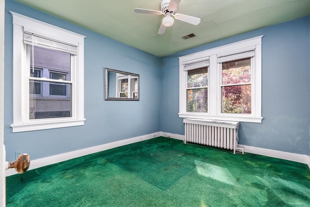 empty room featuring radiator, ceiling fan, and dark carpet