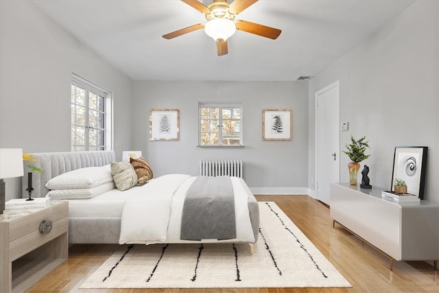 bedroom featuring light hardwood / wood-style flooring, multiple windows, radiator heating unit, and ceiling fan