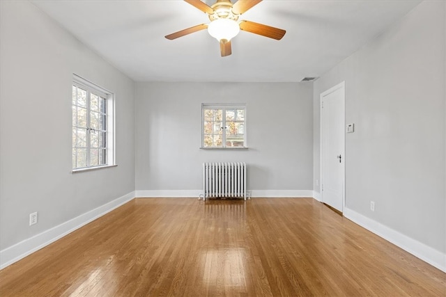 empty room featuring a wealth of natural light, ceiling fan, hardwood / wood-style flooring, and radiator