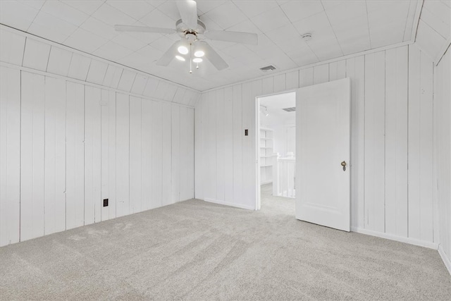 carpeted empty room featuring ceiling fan and wood walls