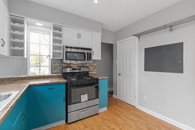 kitchen featuring appliances with stainless steel finishes, blue cabinets, white cabinetry, light hardwood / wood-style floors, and decorative backsplash