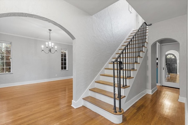 stairs with crown molding, an inviting chandelier, and hardwood / wood-style floors