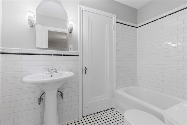 bathroom featuring tiled shower / bath, tile walls, and toilet