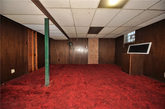 basement featuring wooden walls, a drop ceiling, and carpet flooring