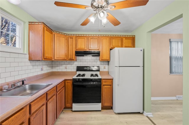 kitchen featuring white appliances, sink, backsplash, light hardwood / wood-style floors, and ceiling fan