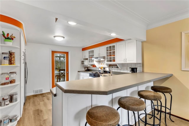 kitchen featuring gas stove, kitchen peninsula, a breakfast bar, white cabinetry, and light wood-type flooring