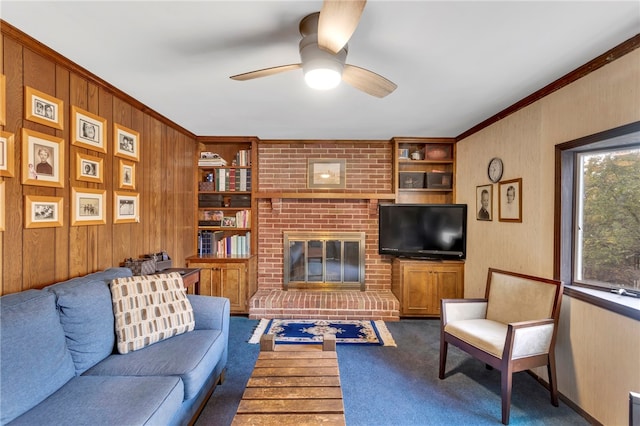 carpeted living room with a brick fireplace, ornamental molding, built in features, and ceiling fan