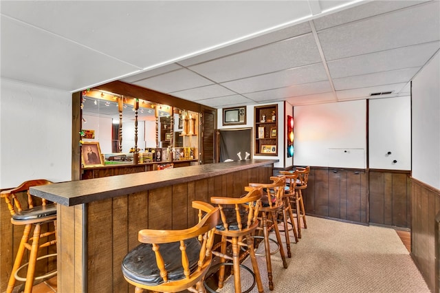 bar with wooden walls, light carpet, and a paneled ceiling